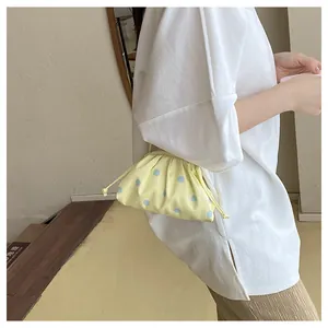 Stylish yellow pleated dumpling bag with blue polka dots shown as a detail on a model