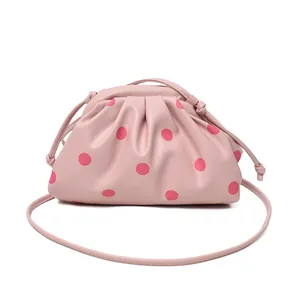 Pink pleated dumpling crossbody bag with red polka dots and adjustable shoulder strap.