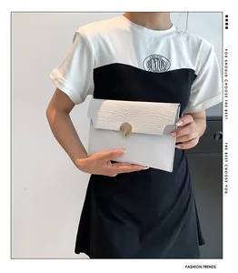 Detail view of a white stone texture envelope clutch bag held by a model in casual wear