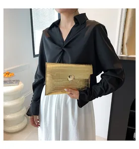 Elegant gold crocodile texture envelope clutch bag held by a model in a stylish outfit.