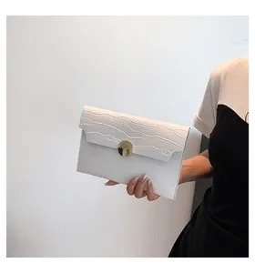 White crocodile embossed envelope clutch bag with gold round clasp held by model.