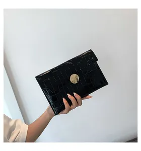 Close-up of black stone-patterned envelope clutch with golden circular metal clasp.