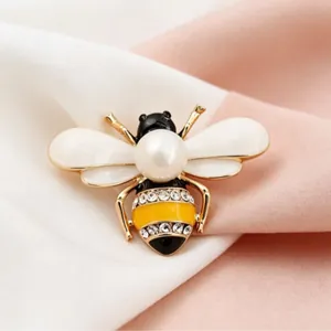 Elegant insect bee brooch with pearl and rhinestone accents on soft fabric background.