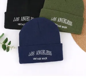 Close-up of three knitted beanies in black, green, and navy with white embroidery.
