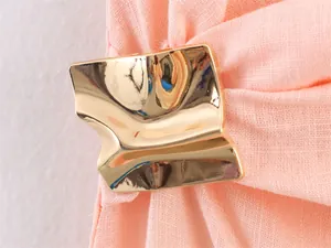 Close-up of the irregular gold metallic clasp on the asymmetric peach midi dress