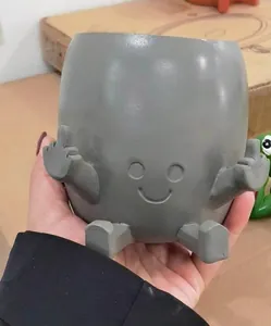 Close-up of grey resin plant pot featuring a humorous middle finger character design