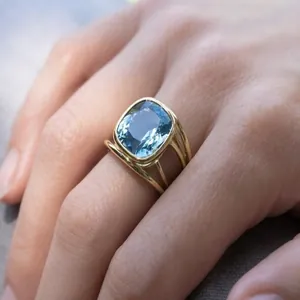 Elegant gold-finish ring featuring a large square-cushion blue gemstone on finger.