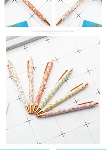 Close-up of floral ballpoint pens with rose gold accents on white grid background