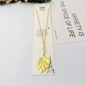 Gros plan d'un pendentif en feuille de ginkgo dorée sur une fine chaîne en inox.