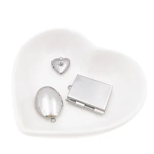 DIY stainless steel photo locket pendants in heart, oval and square shapes on white dish