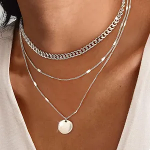 Close-up view of a layered silver curb chain necklace with a circular coin pendant