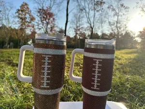 Close-up of 40oz stainless steel tumblers with football rhinestone design in sunlight