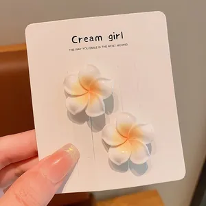 Close-up detail of white plumeria flower hair clips on a Cream girl display card