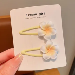 Detail view of two sweet white frangipani flower hair clips on a display card.