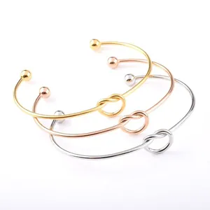 Close-up of three minimalist knot cuff bangles in gold, rose gold, and silver finish