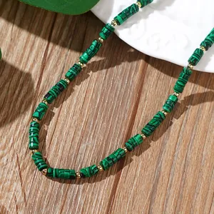 Détail de perles cylindriques vertes style malachite et séparateurs dorés sur bois.