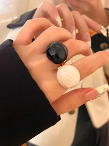 Close-up detail of oversized glossy black and marbled white round enamel rings worn on fingers