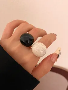 Detailed view of oversized black and marbled white resin eggshell rings on a finger