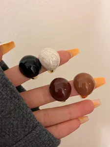 Close-up view of round eggshell enamel rings in chocolate and caramel colors worn on fingers