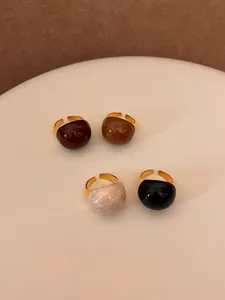 Close-up of four glossy oval resin rings with gold adjustable bands in caramel and chocolate