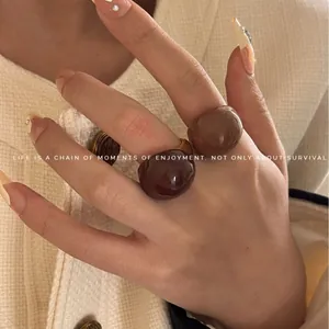Set of chunky chocolate and caramel round rings worn on finger with cream blazer background