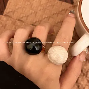 Retro chic round enamel open rings in glossy black and white marble textures on a hand.