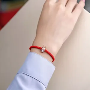 Close-up of a red cord bracelet featuring a rose gold rabbit charm with a sparkling stone