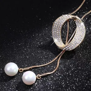 Close-up of elegant gold sweater chain with sparkling rhinestone pendant and twin pearls