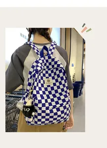 Detail view of a blue and white checkerboard schoolbag featuring a fuzzy ball keychain