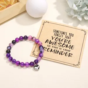 Close-up of a purple beaded stone bracelet with heart charm on a motivational card
