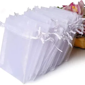 A large stack of white organza drawstring gift bags for jewelry and wedding favors