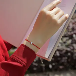 Close-up detail shot of a minimalist red string bracelet with a brilliant moissanite stone