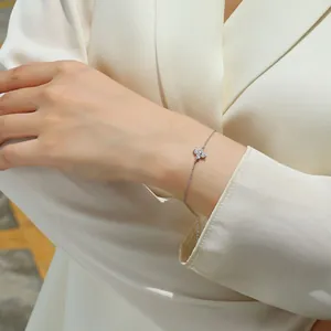 Close-up detail of a silver moissanite four-leaf flower bracelet worn on a woman's wrist