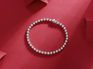 A high-quality detail view of a silver bezel-set moissanite tennis bracelet on red.