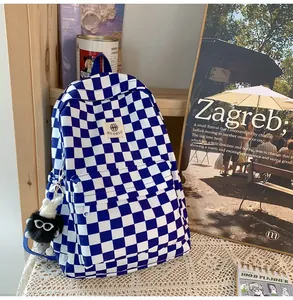 Detail view of a blue and white checkered backpack featuring a cute black fuzzy charm.