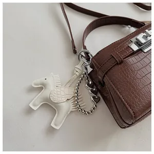 Detailed macro view of a brown crocodile pattern handbag with an elegant white horse charm
