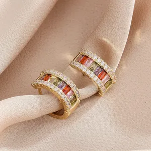 Close-up of gold-plated huggie hoop earrings with colorful baguette zircons on luxury satin.