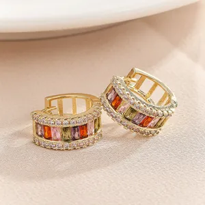 Close-up detail of luxury gold-plated huggie hoop earrings with multi-color baguette zircons