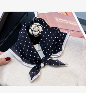 Close-up of a black and white polka dot silk scarf tied on a white knitted sweater.