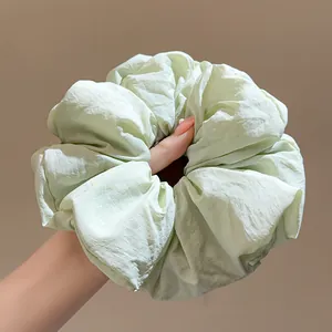 Large light green fabric scrunchie hair tie held by hand against neutral background