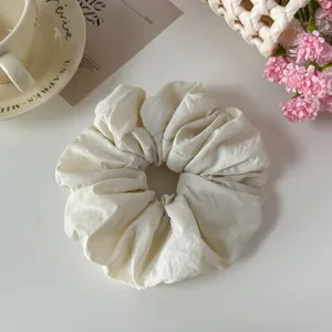 Macro view of a cream textured fabric scrunchie showing soft wrinkles and pleats detail
