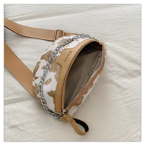 Détail d'un sac de poitrine vintage imprimé vache avec bandoulière large et chaîne.