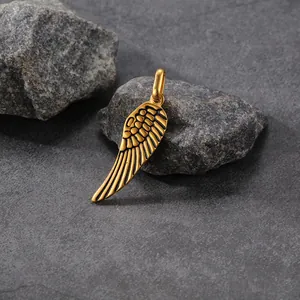 Detailed view of a gold-colored stainless steel angel wing pendant on stone.