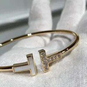 Primer plano de un brazalete de doble T dorado con nácar y piedras engastadas en pavé