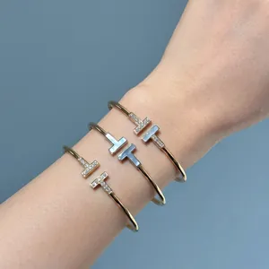 Elegante conjunto de brazaletes abiertos doble T con nácar y cristaux pavé en la muñeca