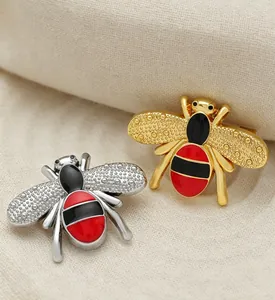 Close-up of elegant gold and silver bee brooches featuring red and black enamel finish