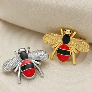 Pair of cartoon bee brooches in gold and silver finish with red enamel details.