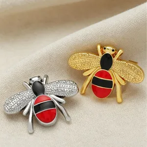 Enamel bee brooch pins in gold and silver finishes presented on a soft fabric background