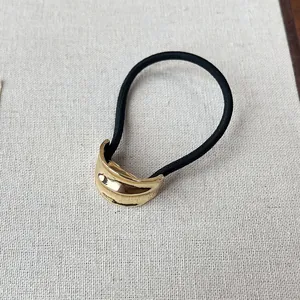 Close-up detail of a minimalist gold metal crescent hair tie on a textured beige fabric background.