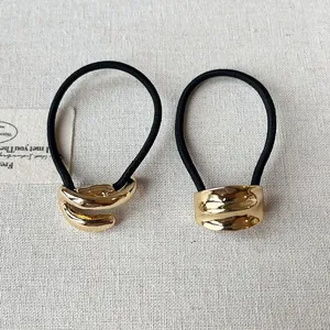 Macro detail of elegant gold-toned metal cuff ponytail holders on a white linen surface